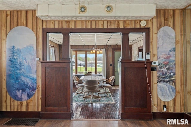 foyer featuring wooden walls, wood finished floors, an inviting chandelier, and ornate columns