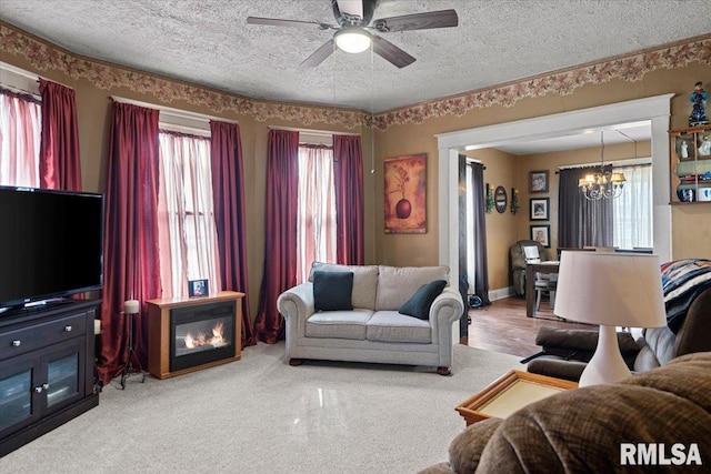 living room featuring ceiling fan with notable chandelier, baseboards, and a textured ceiling