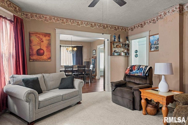 carpeted living room featuring ceiling fan with notable chandelier and a textured ceiling