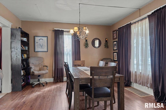 dining space featuring baseboards, visible vents, a chandelier, and wood finished floors