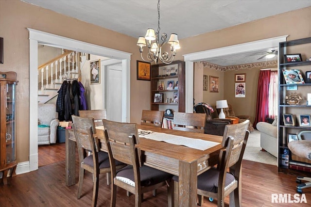 dining area featuring ceiling fan with notable chandelier, stairs, and wood finished floors
