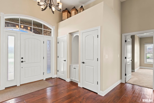 entryway with a towering ceiling, dark wood-type flooring, baseboards, and a chandelier
