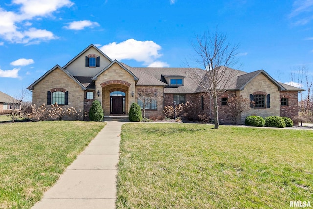 french country inspired facade with stone siding, a shingled roof, brick siding, and a front yard