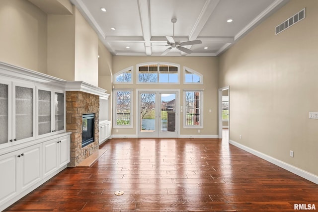 unfurnished living room with dark wood-style flooring, visible vents, baseboards, ceiling fan, and a stone fireplace