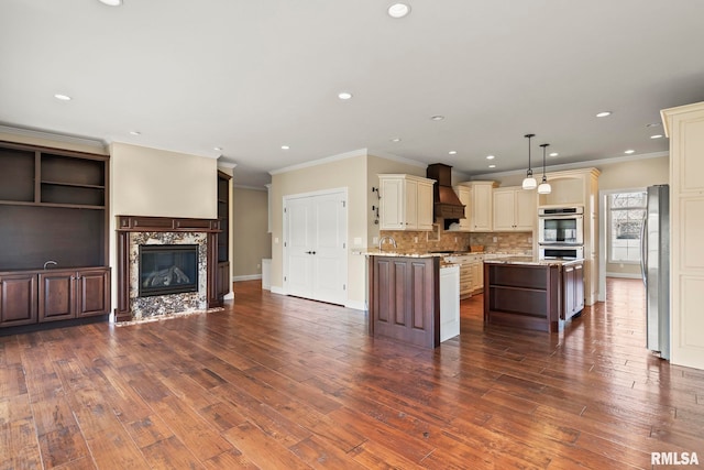 kitchen featuring a fireplace, stainless steel appliances, a kitchen island, custom range hood, and cream cabinets
