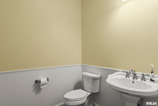 bathroom featuring wainscoting, toilet, and a sink