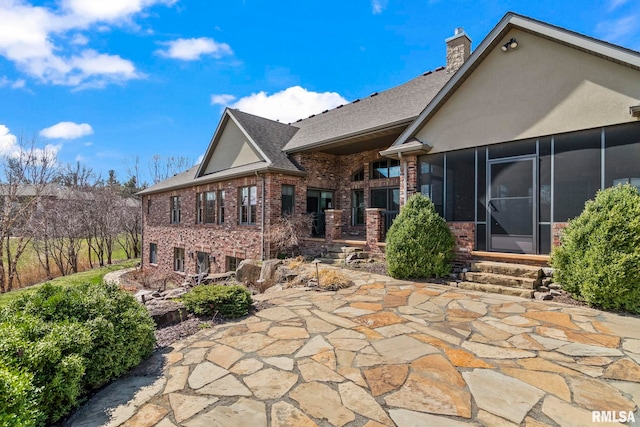 back of house featuring a chimney, a sunroom, stucco siding, brick siding, and a patio area