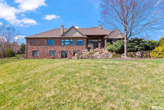 back of property with a chimney, brick siding, and a yard