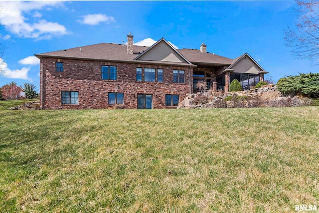 back of property featuring brick siding, a sunroom, a yard, and a chimney