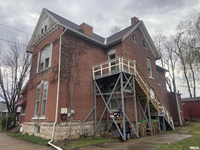 back of house featuring stairs, a chimney, and brick siding