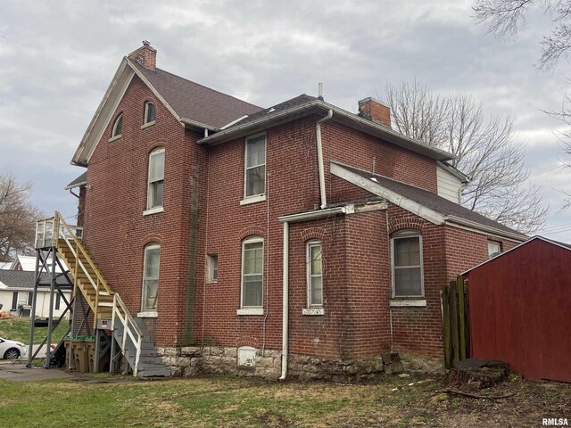 view of side of home with brick siding, stairway, and a chimney
