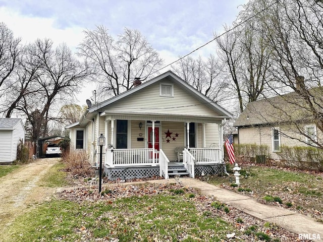 bungalow featuring a chimney, a porch, a carport, and dirt driveway
