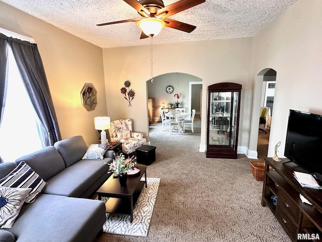 carpeted living room with arched walkways, a textured ceiling, and a ceiling fan