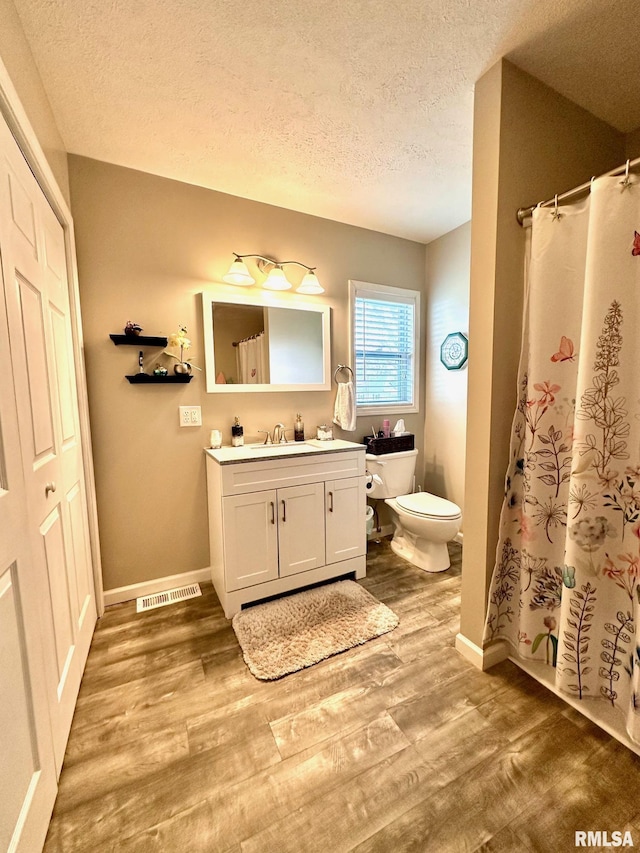 full bath with vanity, toilet, a textured ceiling, visible vents, and wood finished floors