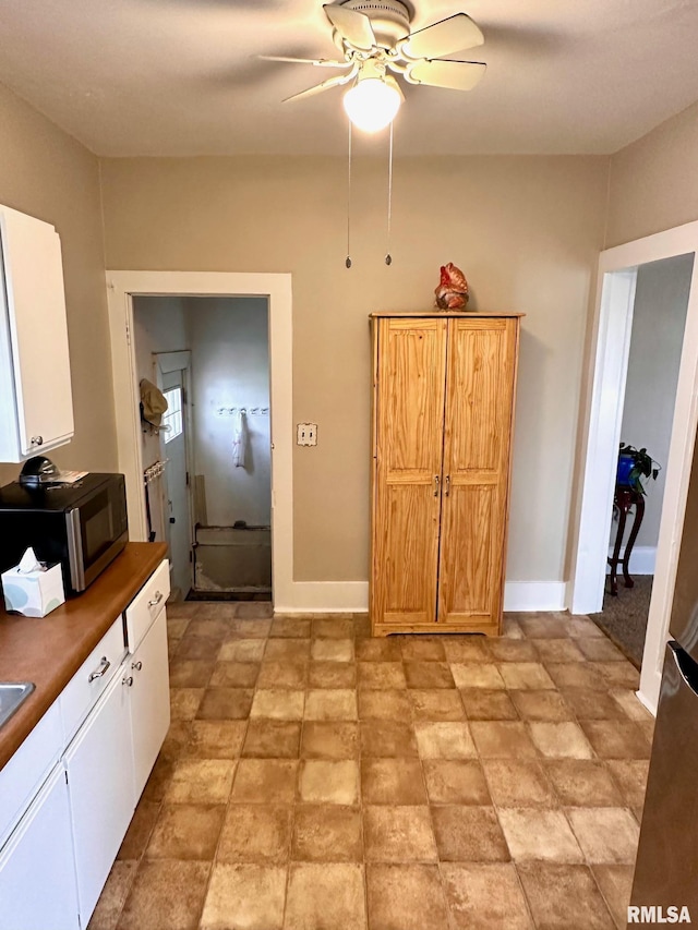 interior space featuring baseboards, white cabinetry, dark countertops, and a ceiling fan