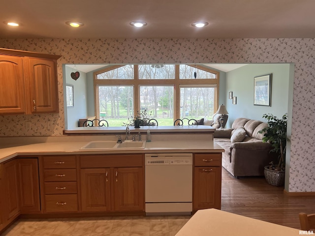 kitchen featuring light countertops, a sink, open floor plan, white dishwasher, and wallpapered walls