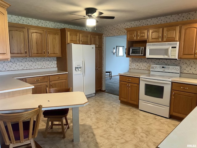 kitchen featuring a ceiling fan, a breakfast bar area, light floors, white appliances, and wallpapered walls