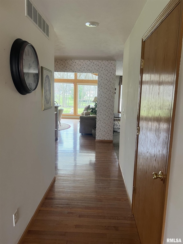 hallway with baseboards, visible vents, and wood finished floors