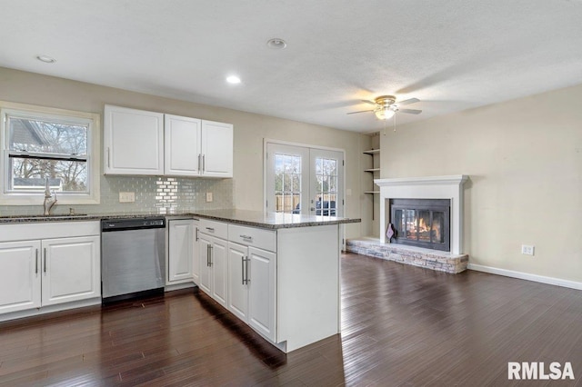 kitchen with a peninsula, a ceiling fan, dark stone countertops, dishwasher, and a sink