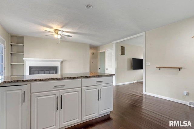 kitchen with white cabinets, dark stone countertops, baseboards, and ceiling fan