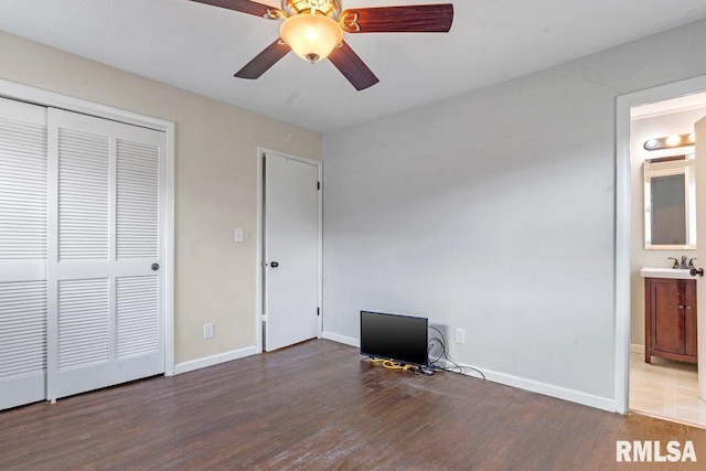 unfurnished bedroom with a closet, baseboards, ensuite bathroom, a ceiling fan, and wood finished floors