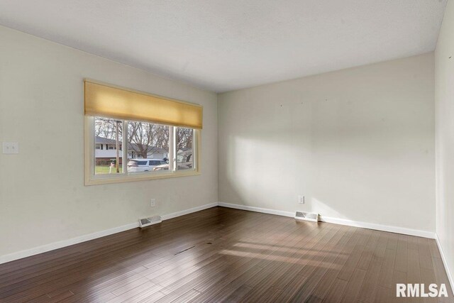 unfurnished room with visible vents, baseboards, and dark wood finished floors