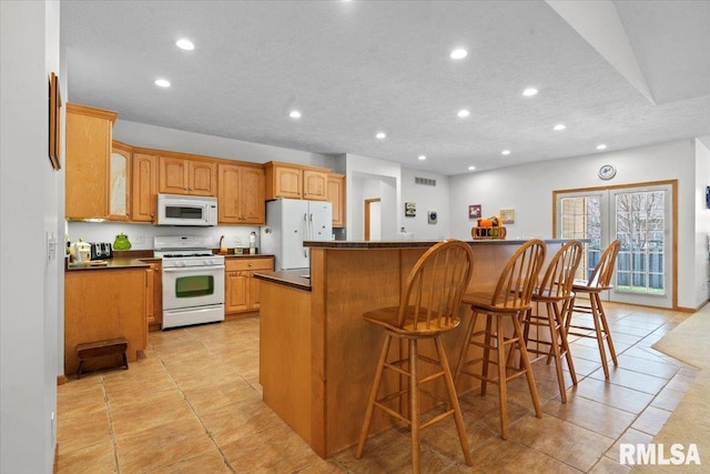 kitchen featuring recessed lighting, dark countertops, a center island, and white appliances