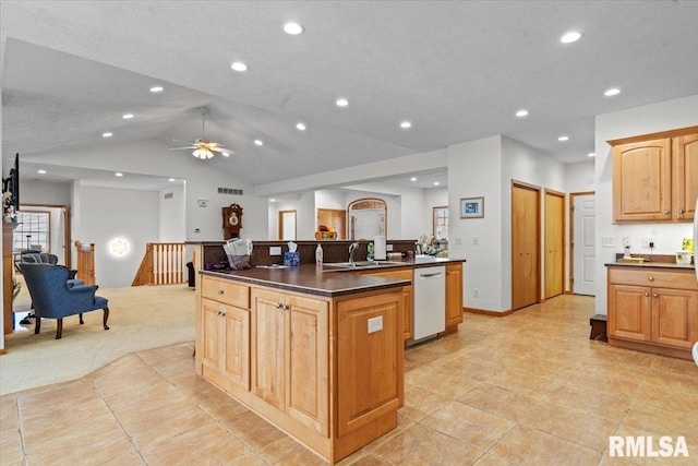 kitchen with vaulted ceiling, a sink, dark countertops, an island with sink, and white dishwasher