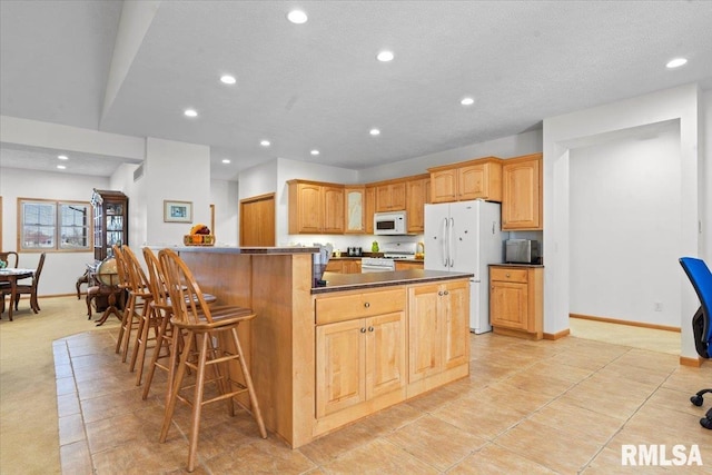 kitchen with a breakfast bar, baseboards, white appliances, dark countertops, and recessed lighting