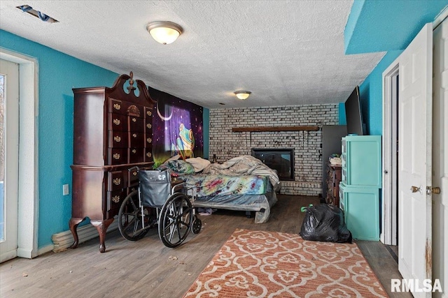bedroom with a textured ceiling, a fireplace, and wood finished floors
