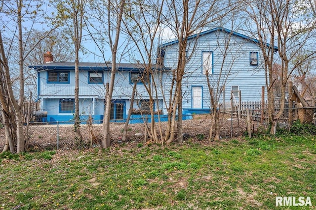 rear view of house featuring a lawn, fence, and a chimney