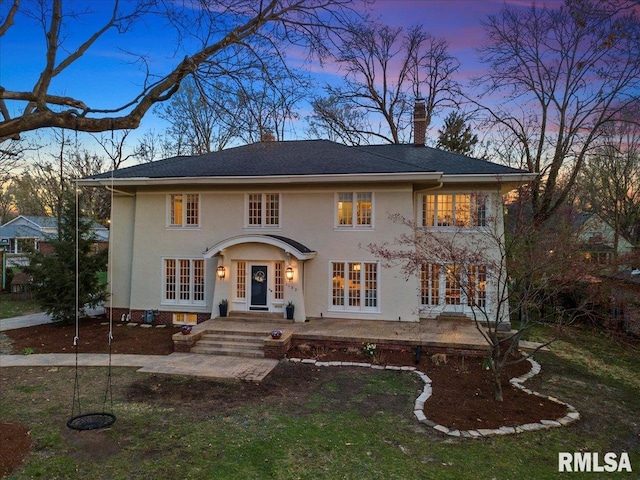colonial-style house featuring a patio, french doors, stucco siding, and a chimney