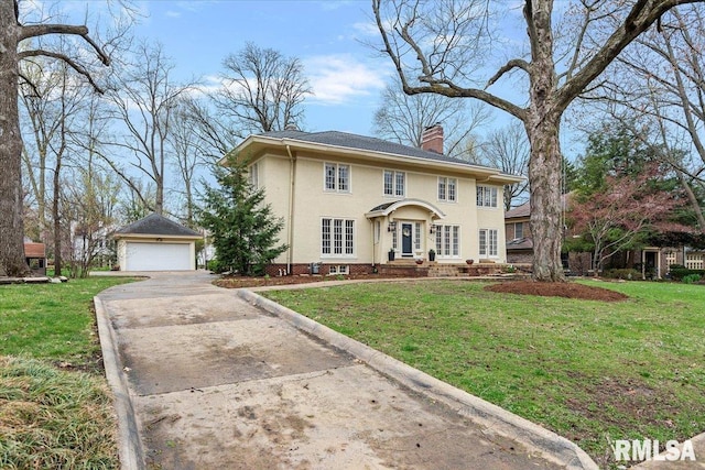 colonial inspired home featuring a detached garage, a chimney, an outdoor structure, stucco siding, and a front lawn