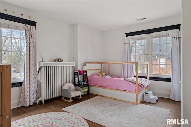 bedroom with crown molding, visible vents, multiple windows, and wood finished floors
