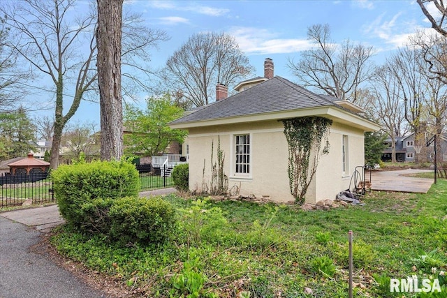 view of side of property featuring a yard, a chimney, fence, and stucco siding