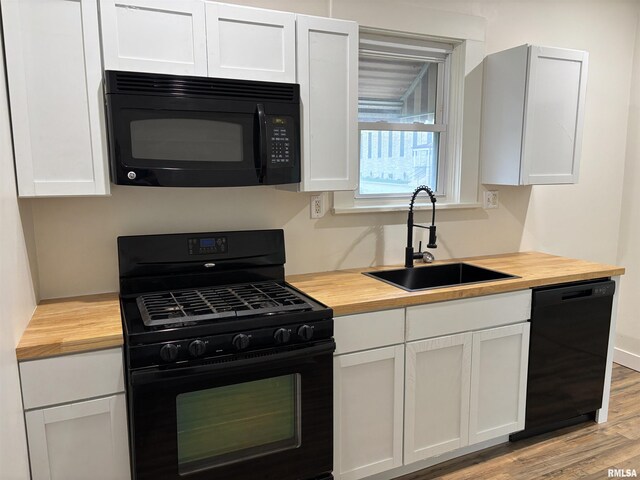 kitchen featuring butcher block countertops, white cabinetry, black appliances, and a sink
