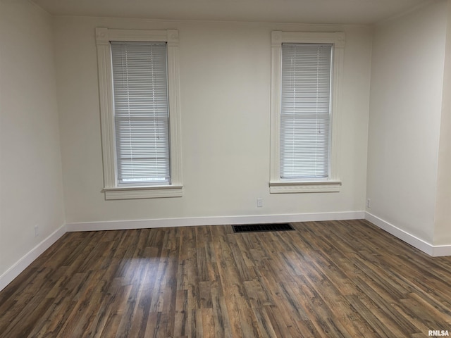 empty room featuring baseboards, dark wood-style floors, visible vents, and a healthy amount of sunlight