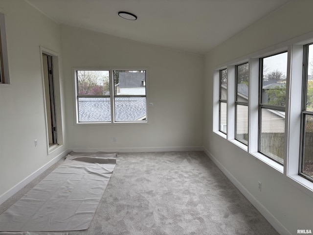 empty room featuring a healthy amount of sunlight, baseboards, lofted ceiling, and light colored carpet