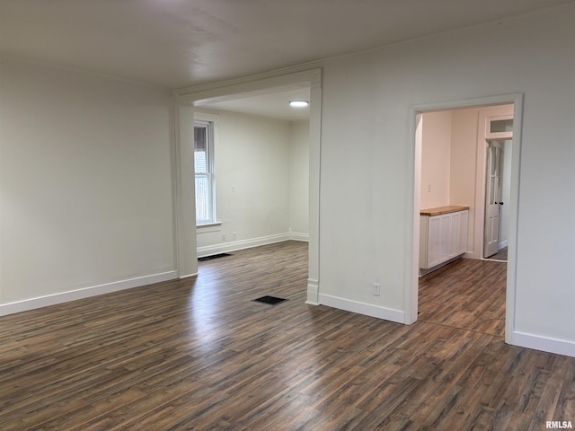 unfurnished room with dark wood-style flooring, baseboards, and visible vents