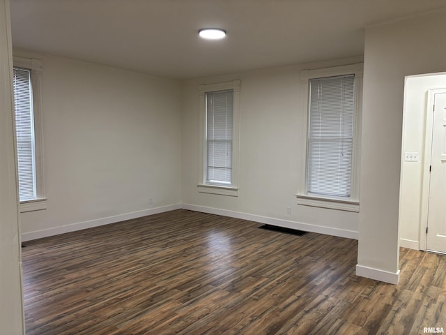 spare room with baseboards, dark wood-style floors, and visible vents
