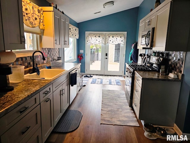 kitchen with a sink, stainless steel appliances, tasteful backsplash, dark countertops, and lofted ceiling