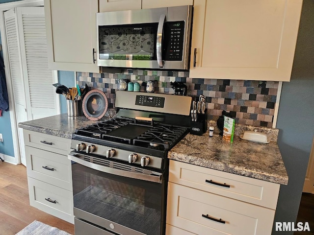 kitchen with dark stone countertops, light wood-style flooring, stainless steel appliances, and tasteful backsplash