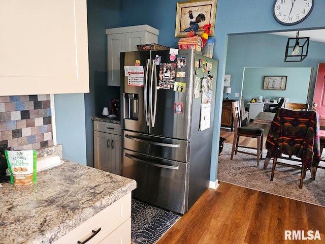 kitchen with white cabinetry, dark wood-style flooring, light stone countertops, stainless steel refrigerator with ice dispenser, and backsplash