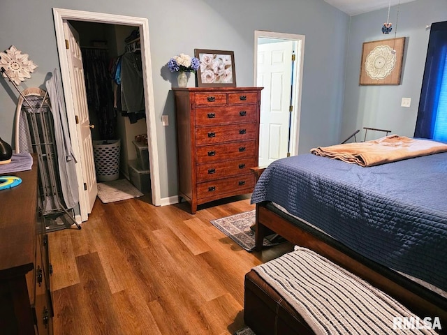 bedroom featuring wood finished floors, a spacious closet, a closet, and baseboards
