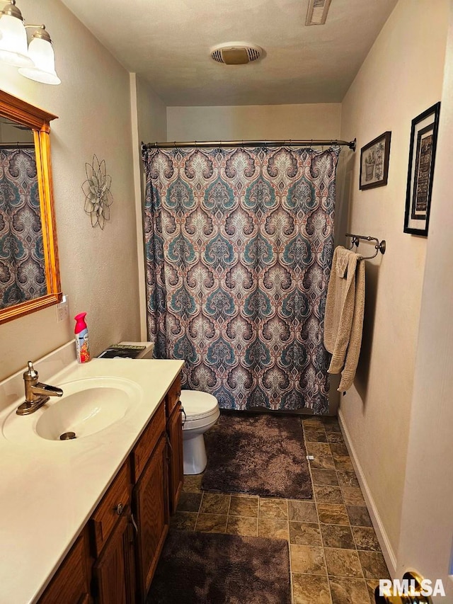 full bath with stone finish floor, toilet, vanity, baseboards, and visible vents