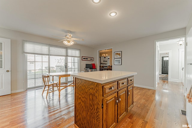 kitchen featuring a center island, light countertops, light wood-type flooring, brown cabinetry, and ceiling fan with notable chandelier