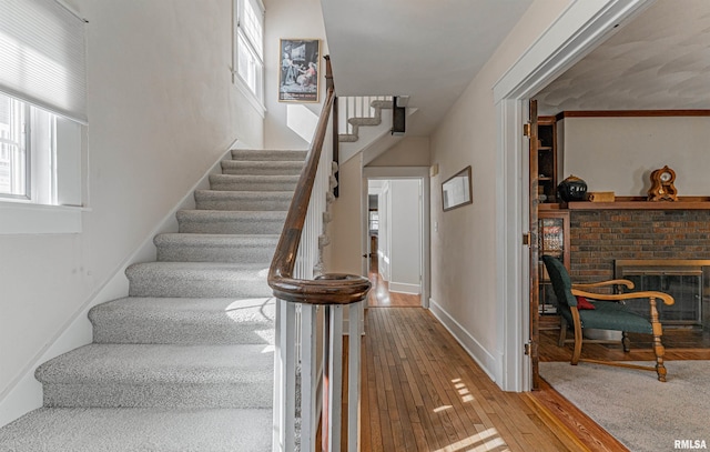 stairway with plenty of natural light, a brick fireplace, baseboards, and hardwood / wood-style floors