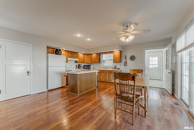 kitchen featuring white appliances, under cabinet range hood, wood finished floors, light countertops, and brown cabinets