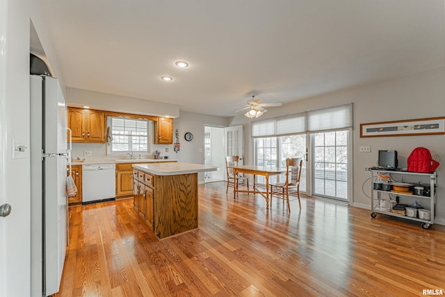 kitchen featuring ceiling fan, white appliances, a center island, light countertops, and light wood finished floors