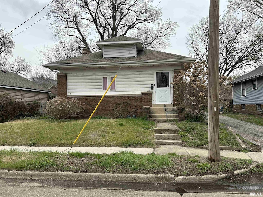 bungalow-style house featuring roof with shingles, brick siding, entry steps, and a front lawn